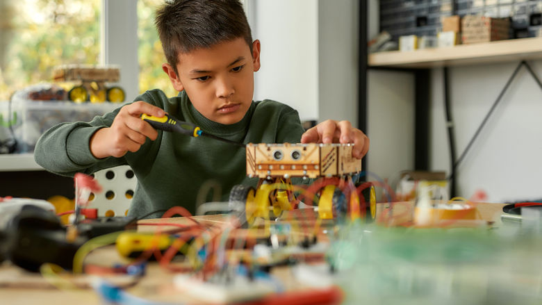 Boy using screwdriver while fixing bolts on a robot vehicle. Smart kids and STEM education.