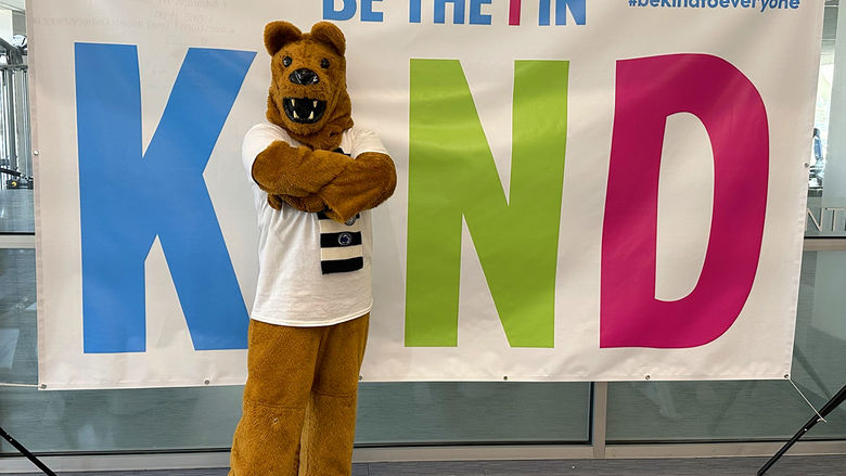 Nittany Lion mascot standing in front of a sign that says Be the I in KIND