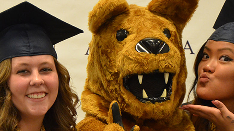 Two recent graduates make kissy faces with the Nittany Lion