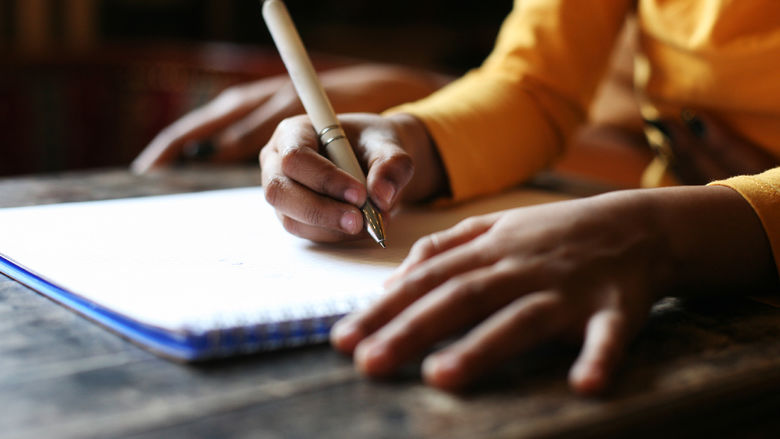 Human hands writing in a notebook using a pencil.