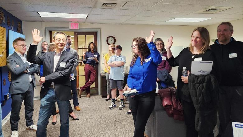 Group of people standing in an office, some have their hands raised. 