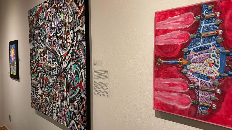 Art gallery wall with three colorful abstract paintings, including bold red, graffiti-style, and vibrant fantasy-themed works.