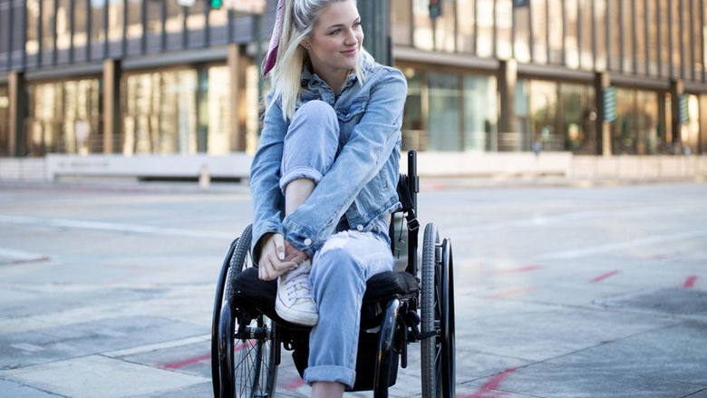 A young woman in a wheelchair with a large city building in the background