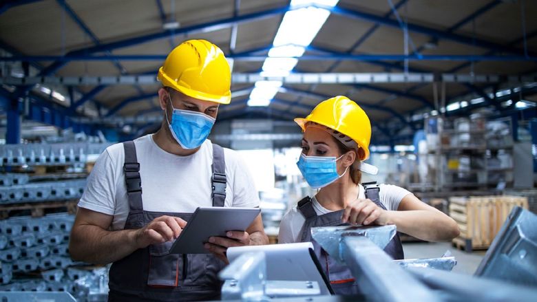 Two masked manufacturing workers in a manufacturing/factory setting