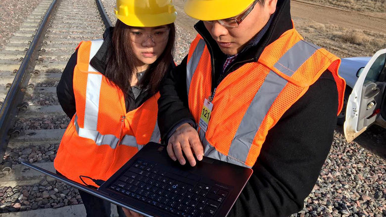 Engineering Professor Hai Huang works with a rail transportation engineering student near railroad tracks