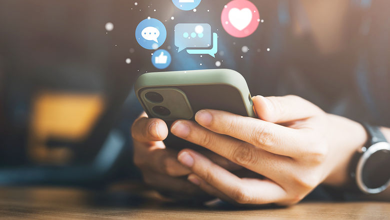 A person holding a phone with icon graphics hovering over the phone. The icons represent various aspects of social media