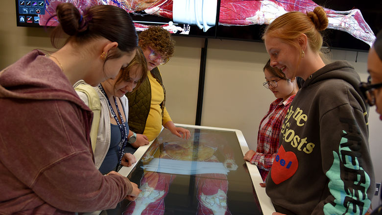 Students gather around a table that details the human anatomy on a touch screen