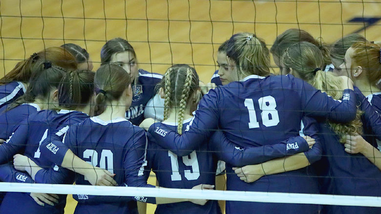 Penn State Altoona's 2023-24 women's volleyball team huddles before a game with a volleyball net in the foreground