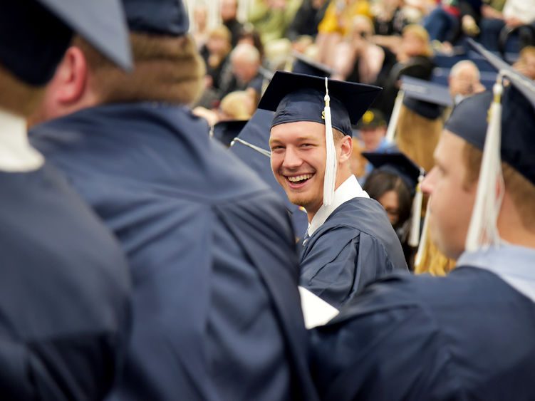 A graduate at Penn State Altoona's spring 2022 commencement ceremony spots the campus photographer and smiles for a photo