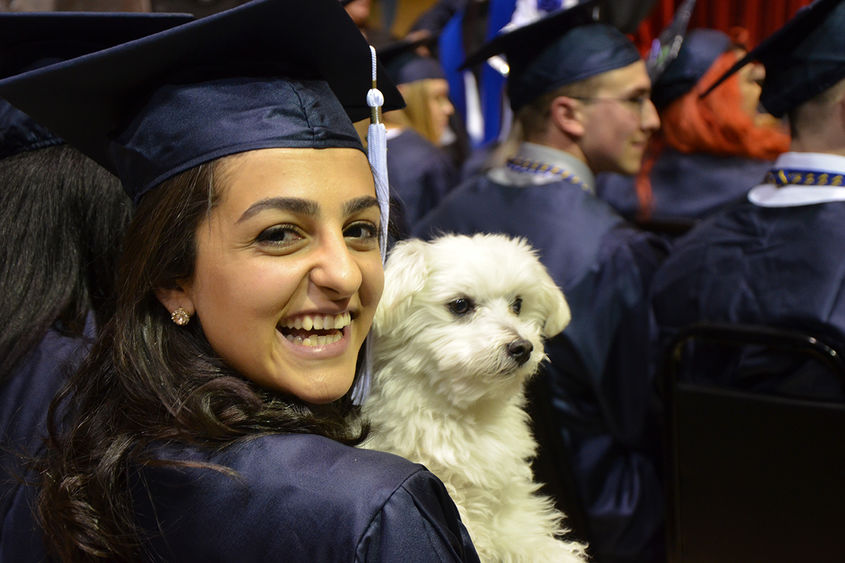A graduate sits with her pet dog at spring 2018 commencement ceremony at Penn State Altoona