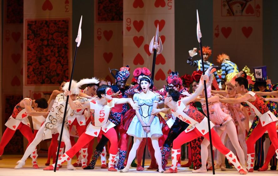 A dancer resembling Alice is surrounded by dancers dressed as playing cards and flamingoes.