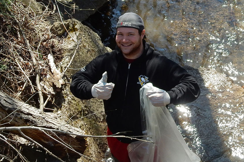 A Penn State Altoona gives a thumbs up while collecting trash along Spring Run