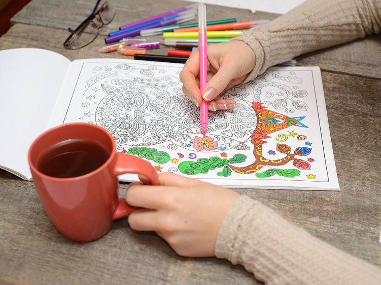 Woman coloring an adult coloring book and drinking tea