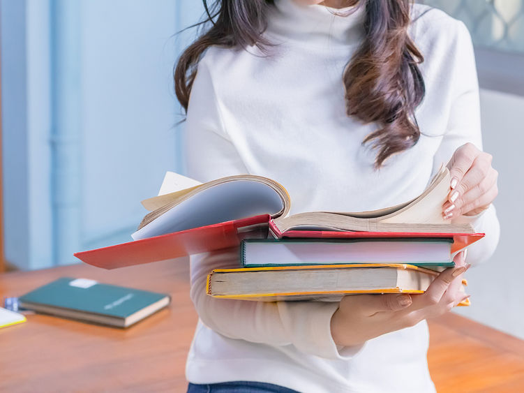 A student reads a book stacked on top of other books.