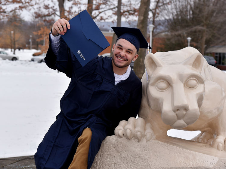 A recent graduate poses with at the Nittany Lion Shrine following commencement