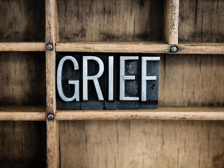 The image shows the word GRIEF spelled out in metal letterpress blocks placed within a wooden compartment, evoking a strong, somber emotion.