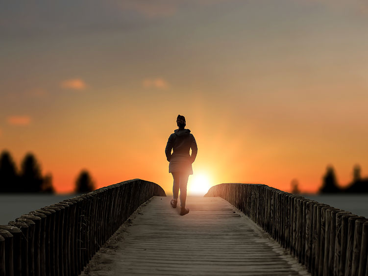 a woman stands on bridge over a lake at sunset