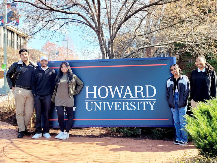 Five students pose in front of a Howard University sign