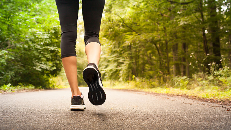 The feet and legs of a woman walking on a path surrounded by woods.