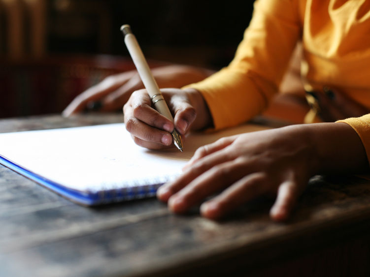 Human hands writing in a notebook using a pencil.