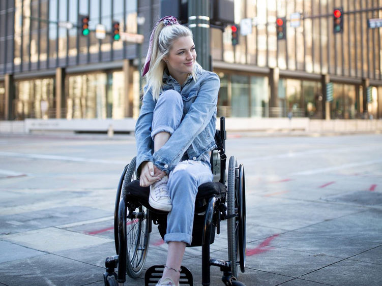 A young woman in a wheelchair with a large city building in the background