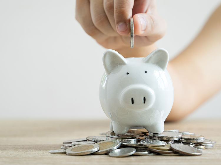 A hand putting a coin in a piggy bank