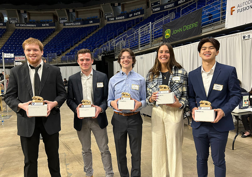 Five students, Dale Miller, Kieran Meehan, Taylor Casavant, Sydney McKernan and James Fong, stand in a row, all holding award statues of the Penn State Nittany Lion