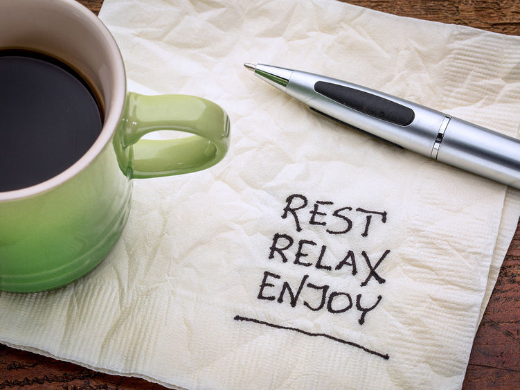 Rest, relax, and enjoy written on a napkin with a cup of coffee in the corner