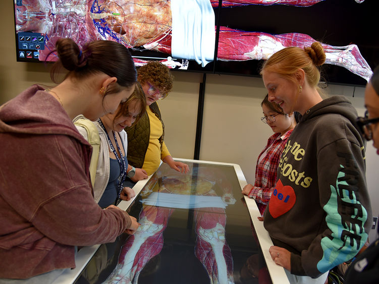 Students gather around a table that details the human anatomy on a touch screen