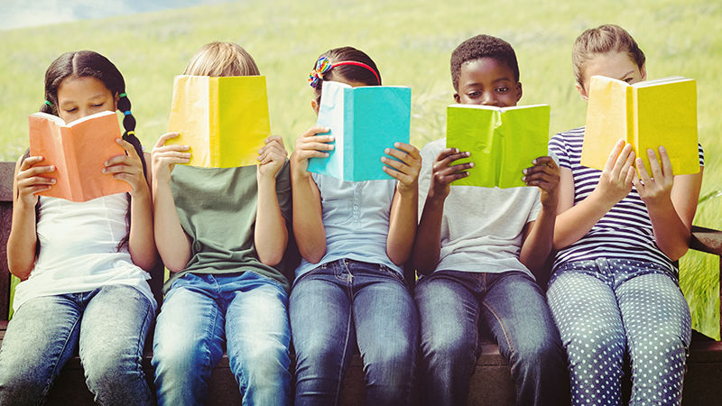 five children sitting in a row reading books with brightly colored covers